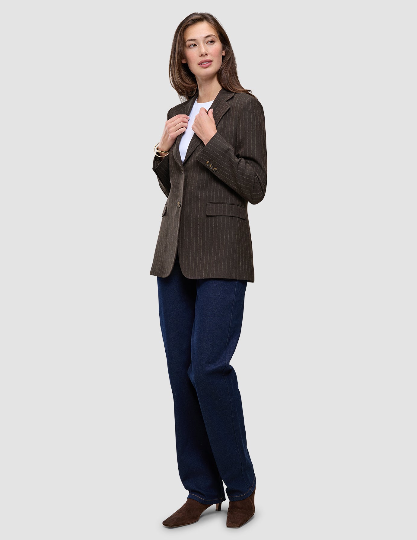 En kvinna klädd i en Women Serene Blazer Regular Walnut Herringbone, en vit t-shirt och mörkblå jeans.